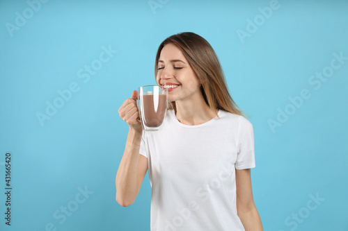 Young woman drinking chocolate milk on light blue background