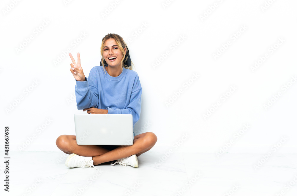 Young blonde Uruguayan girl with the laptop isolated on white background smiling and showing victory sign Young blonde Uruguayan girl with the laptop isolated on white background smiling and showing victory sign