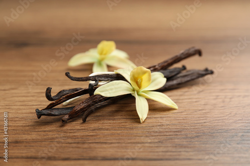 Aromatic vanilla sticks and flowers on wooden table, closeup