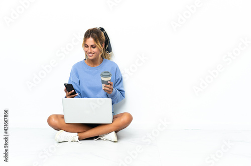 Young blonde Uruguayan girl with the laptop isolated on white background holding coffee to take away and a mobile