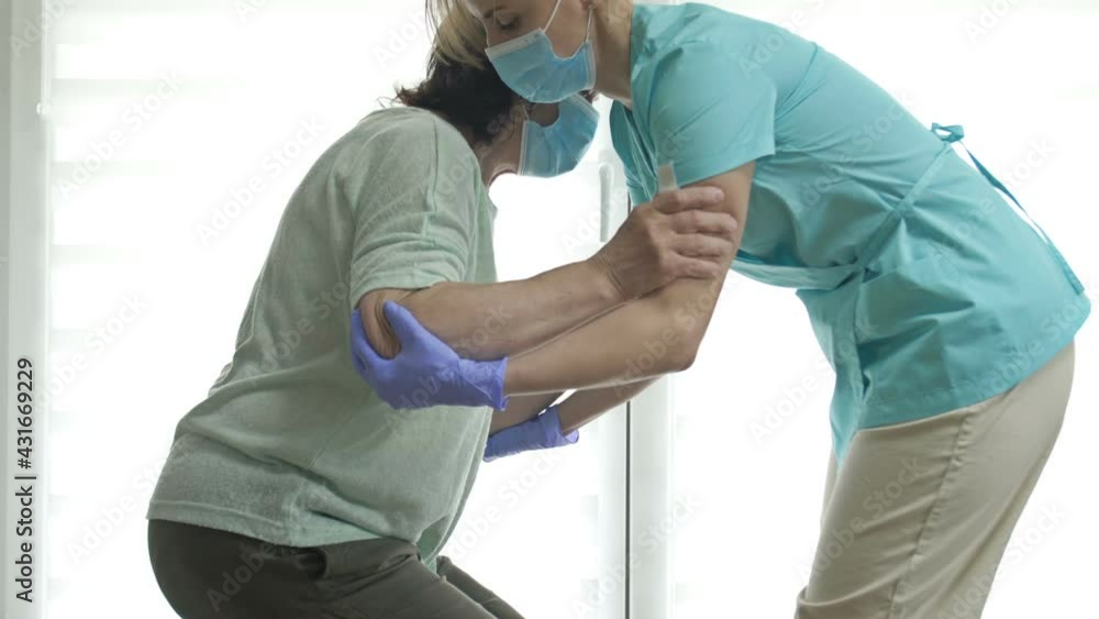 Doctor or nurse is helping an elderly woman to get to her feet. Recovering from injury, surgery, or stroke. Doctor or nurse is helping an elderly woman to get to her feet. Recovering from injury, surgery, or stroke.
