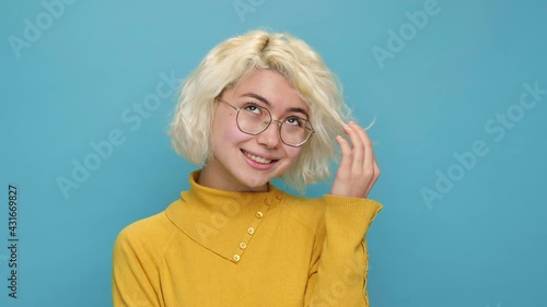 Portrait coquettish cute asian young woman face close up twists lock of curly hair at her face embarrassed smiling looks at camera on blue background. Teen girl feel happy Positive emotions Lifestyle