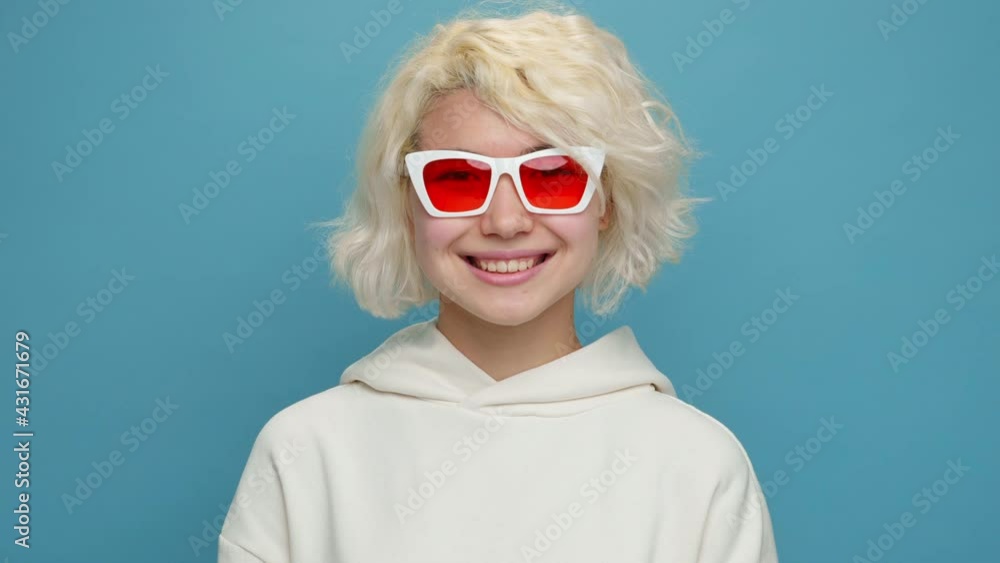 Cheerful young asian woman face close up showing OK sign smiling with her hands gesture body language looking at camera wearing sunglasses with white curly hair on blue background. Positive emotion Cheerful young asian woman face close up showing OK sign smiling with her hands gesture body language looking at camera wearing sunglasses with white curly hair on blue background. Positive emotion