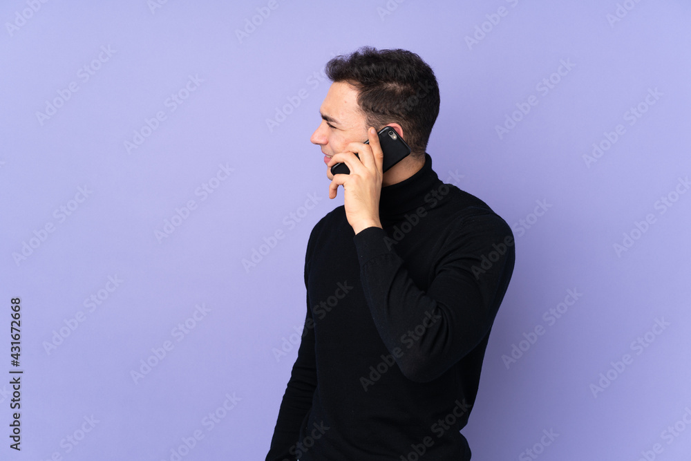 Young caucasian handsome man with turtleneck sweater isolated on purple background keeping a conversation with the mobile phone with someone Young caucasian handsome man with turtleneck sweater isolated on purple background keeping a conversation with the mobile phone with someone
