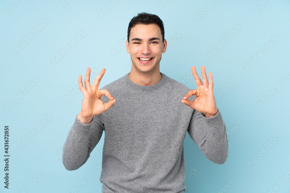 Fototapeta premium Young caucasian handsome man isolated on blue background showing an ok sign with fingers