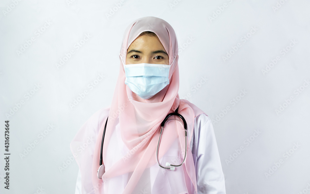 Muslim female doctor wearing headscarf, gown uniform and face mask to protect virus with stethoscope, standing on isolated white background. New Normal, Medical Treatment, Service and Science Concept. Muslim female doctor wearing headscarf, gown uniform and face mask to protect virus with stethoscope, standing on isolated white background. New Normal, Medical Treatment, Service and Science Concept.