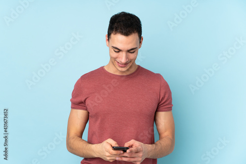 Young caucasian handsome man isolated on blue background sending a message with the mobile