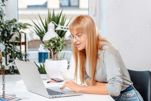 Enthusiastic female entrepreneur sits at table in daytime in modern office