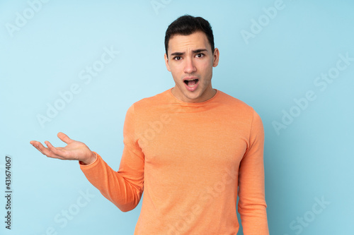 Young caucasian handsome man isolated on blue background making doubts gesture