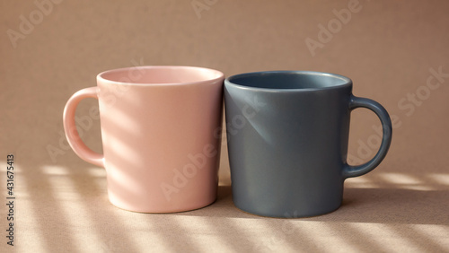 Two cups pink and gray color for coffee, stand on a beige background. A place for text. banner. Coffee day. Valentine's Day. Close-up cups. Minimalism with coffee. Breakfast