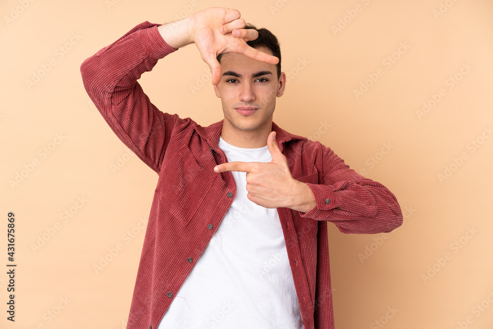 Young caucasian handsome man isolated on beige background focusing face. Framing symbol Young caucasian handsome man isolated on beige background focusing face. Framing symbol