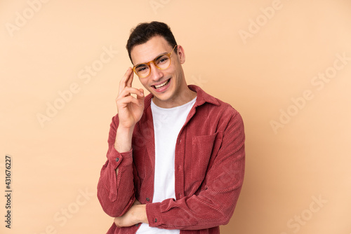 Young caucasian handsome man isolated on beige background with glasses and smiling