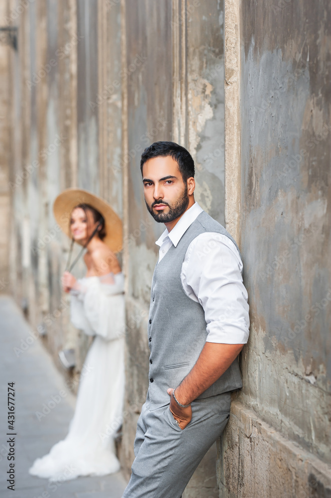 Stylish handsome bearded arab groom in a gray suit. Young couple posing on the street of the old city.
