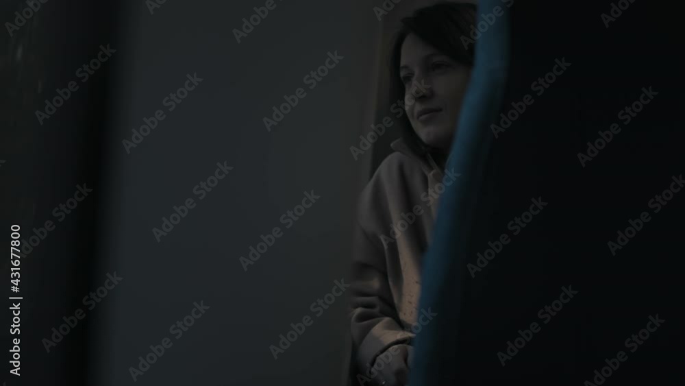 Close-up of young woman in stylish oversize coat and scarf looking out window while riding train at sunset Close-up of young woman in stylish oversize coat and scarf looking out window while riding train at sunset