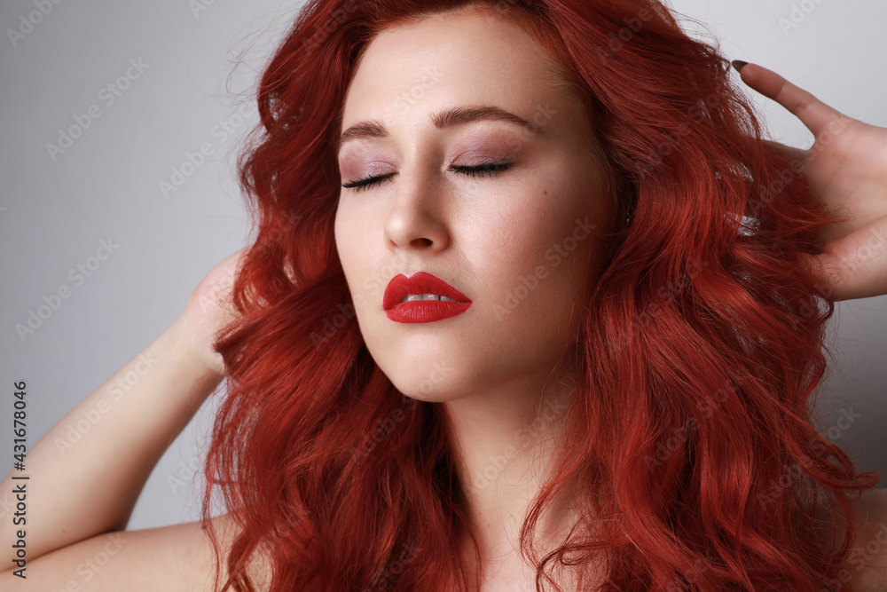 Close-up of beautiful young woman with red hair posing over grey background. Close-up of beautiful young woman with red hair posing over grey background.