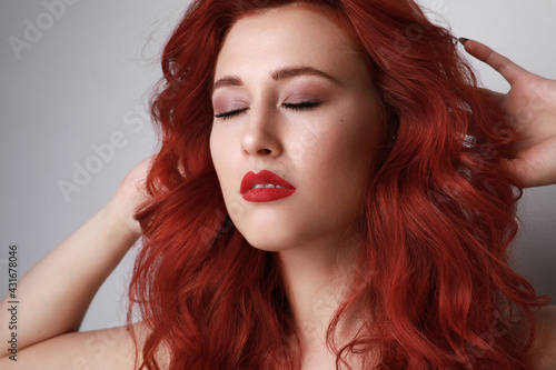 Close-up of beautiful young woman with red hair posing over grey background. 