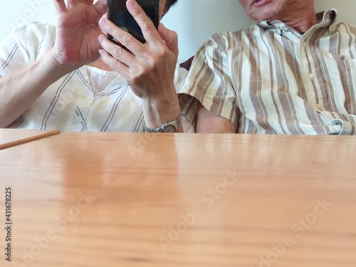 Close up of happy mature old couple's spouse sitting at coffee shop holding mobile phone in hand and having table enjoying life background technology photo