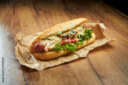 Large hot dog with different fillings, smoked sausage, cheese sauce and cheese on craft paper on a wooden background Fototapet