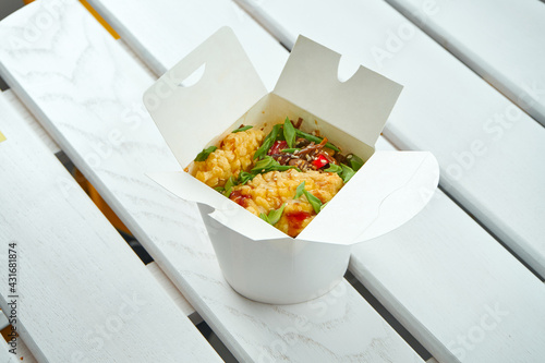 Appetizing Asian wok noodles with vegetables, onions, sauces and chicken in a white delivery box on a white wooden plate. Photo for food delivery