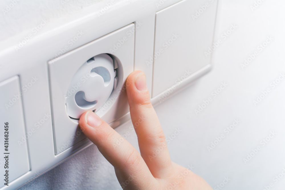 Two Child Fingers Touching A Wall Socket With Safety Plugs - Prevent Child Hazard Concept Two Child Fingers Touching A Wall Socket With Safety Plugs - Prevent Child Hazard Concept