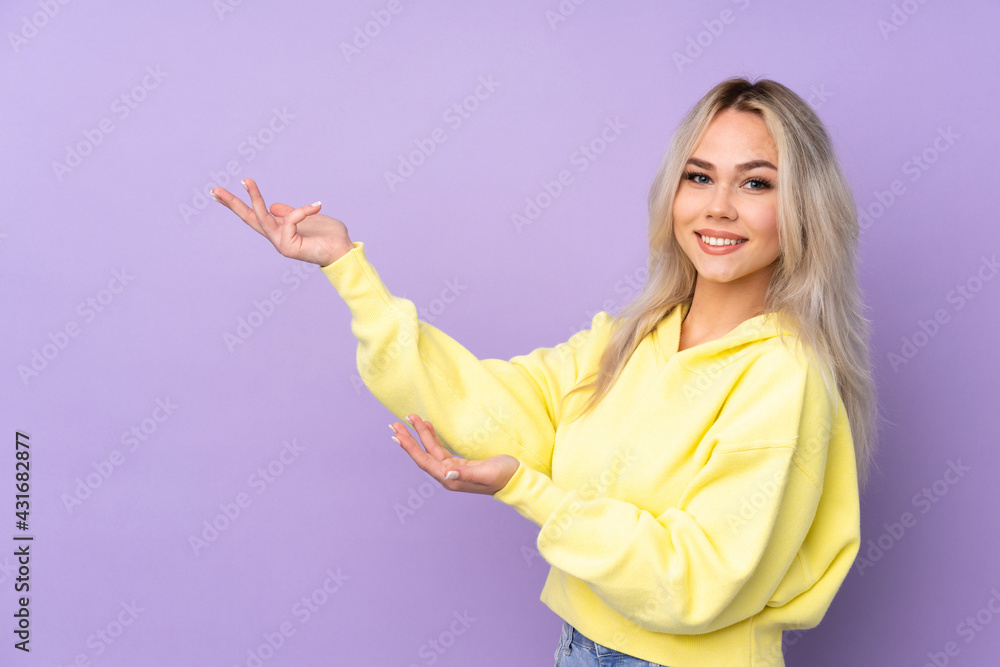 Teenager girl wearing a yellow sweatshirt over isolated purple background extending hands to the side for inviting to come Teenager girl wearing a yellow sweatshirt over isolated purple background extending hands to the side for inviting to come