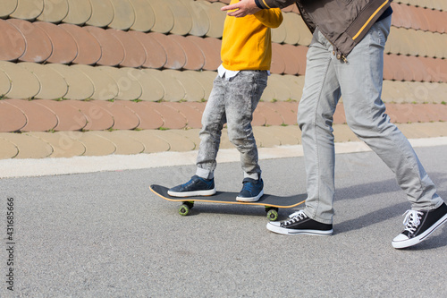 Father is teaching his son to ride a skateboard, outdoors