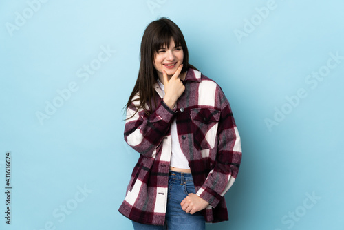 Teenager Ukrainian girl isolated on blue background looking to the side and smiling