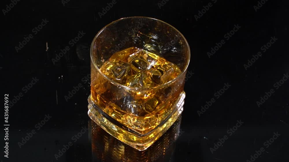 Whiskey. Barman drops ice cubes in the glass with alcohol in slow motion. Glass in reflected surface. 100 fps Whiskey. Barman drops ice cubes in the glass with alcohol in slow motion. Glass in reflected surface. 100 fps