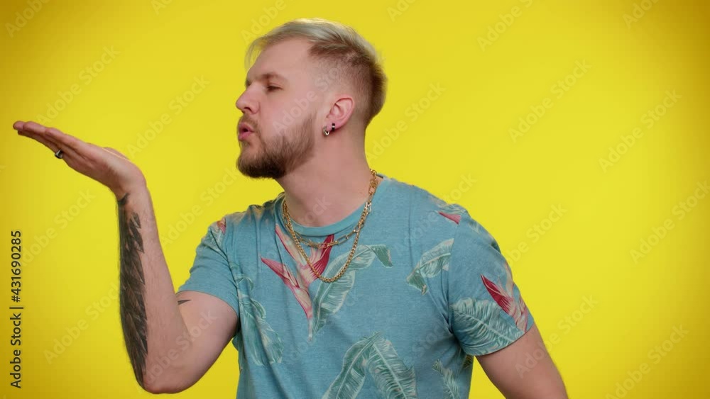 Smiling romantic handsome stylish tourist guy in t-shirt sending lots of air fly kisses looking at camera and smiling, missing you, love confession. Young man. Indoor studio shot on yellow background Smiling romantic handsome stylish tourist guy in t-shirt sending lots of air fly kisses looking at camera and smiling, missing you, love confession. Young man. Indoor studio shot on yellow background