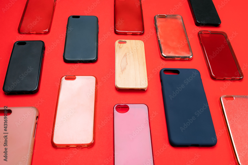 Fototapeta premium Pile of multicolored plastic back covers for mobile phone. Choice of smart phone protector accessories on red background. A lot of silicone phone backs or skins next to each other
