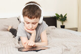 child boy lying on bed with pc tablet with wireless headphones