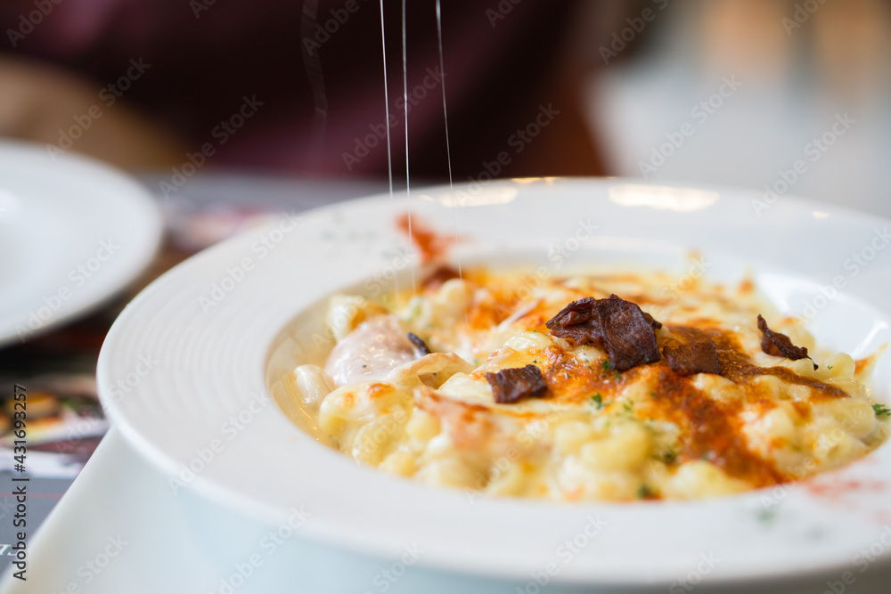 Cheese stretched with fork is being dipped in macaroni cheese with bacon paprika chilli is topping.