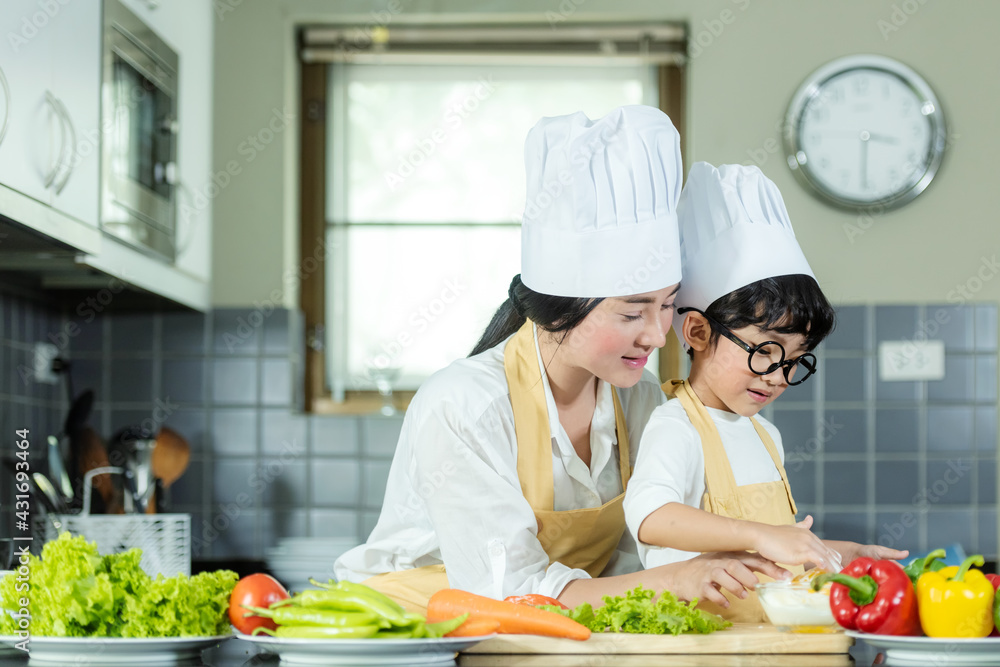Cooking Family. Chef kid boy and mother making and leaning fresh vegetables salad for healthy eat and education. Asian son helping make food, so happy and enjoy Cooking Family. Chef kid boy and mother making and leaning fresh vegetables salad for healthy eat and education. Asian son helping make food, so happy and enjoy