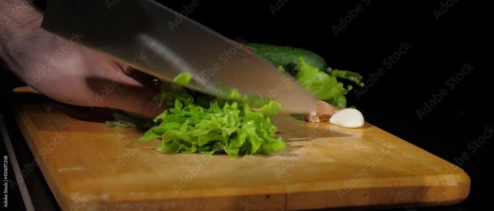 Men's hands cut fresh lettuce with a knife into pieces on cutting board on a black background Men's hands cut fresh lettuce with a knife into pieces on cutting board on a black background