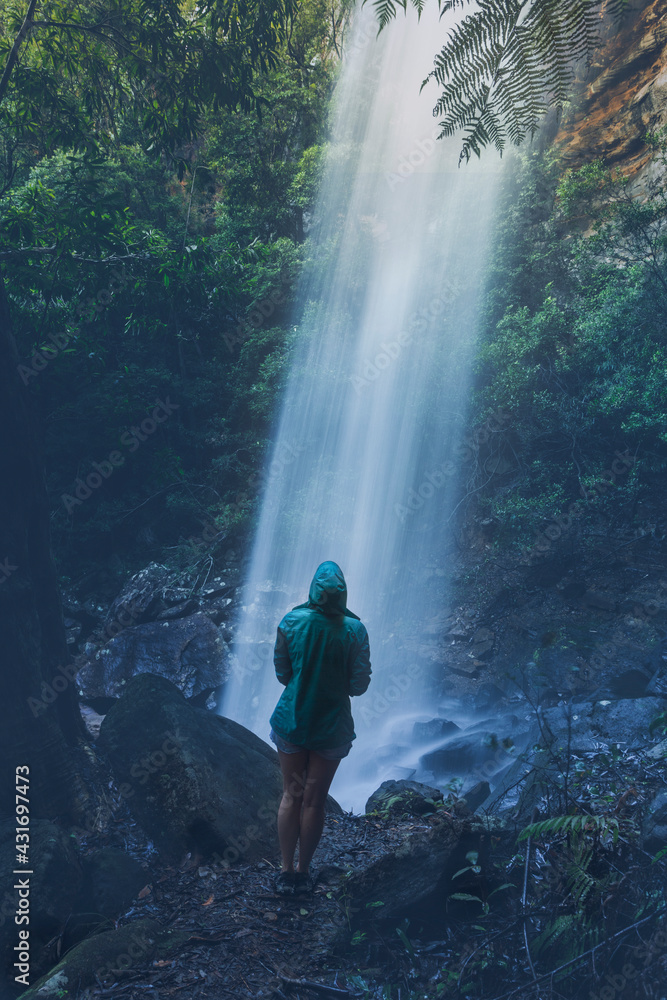 Obraz premium Woman hiker standing below a waterfall after rain