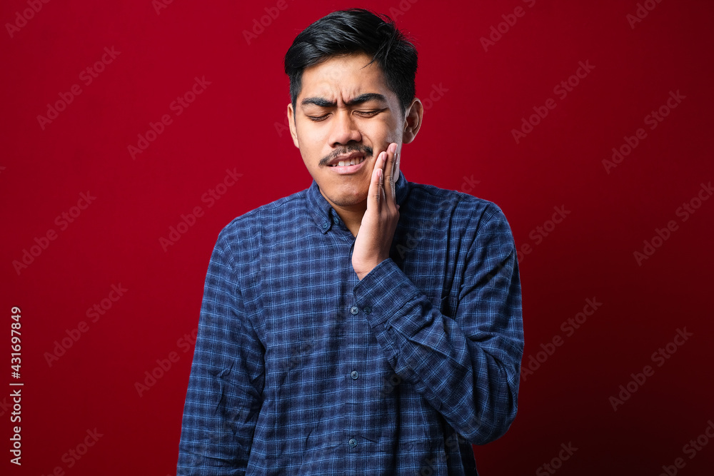 Young handsome man wearing casual shirt standing over isolated red background touching mouth with hand with painful expression Young handsome man wearing casual shirt standing over isolated red background touching mouth with hand with painful expression