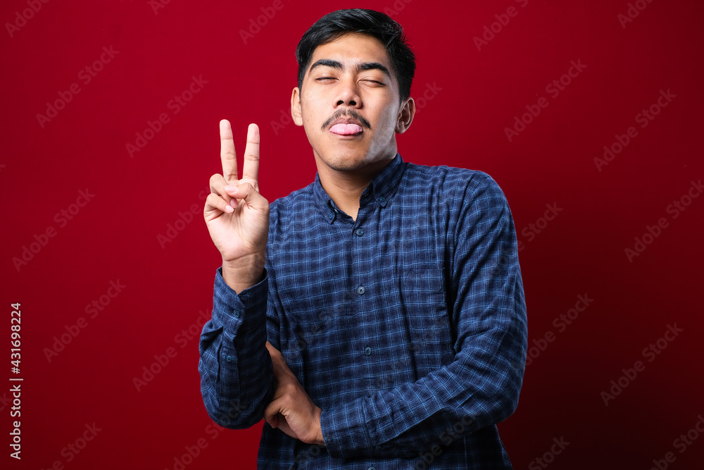 Young handsome asian guy wearing casual shirt standing over red background Doing peace symbol with fingers Young handsome asian guy wearing casual shirt standing over red background Doing peace symbol with fingers