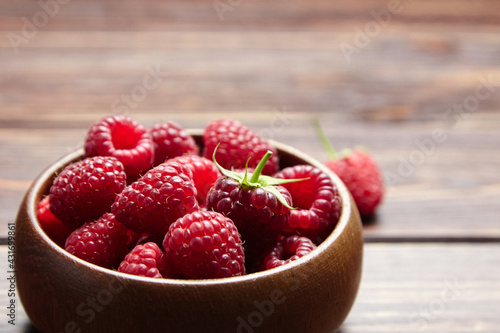 Fresh raspberries in wooden bowl on brown table. Red ripe raspberries, sweet berries