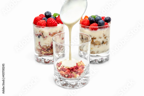 Muesli with yogurt and berries in a glass On a white background. Yogurt is poured from a spoon into a glass. Dessert preparation process. Healthy breakfast. Fitness food. High quality photo