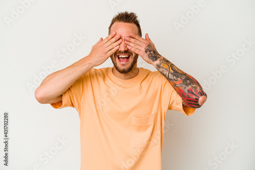 Young tattooed caucasian man isolated on white background covers eyes with hands, smiles broadly waiting for a surprise.