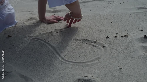Girl drawing a heart on the sand at sunset in a summer love concept