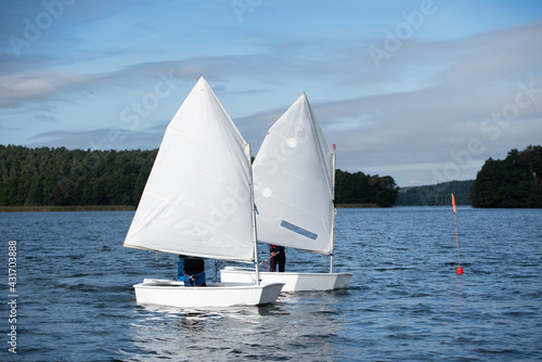 Sailboats of the optimist on the lake with a children's crew on the deck against the backdrop of the forest on a sunny day 