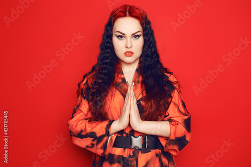 Beautiful girl on a red background. Brunette with red roots of curled hair in a red dress and red lips. Thanks in Japanese.