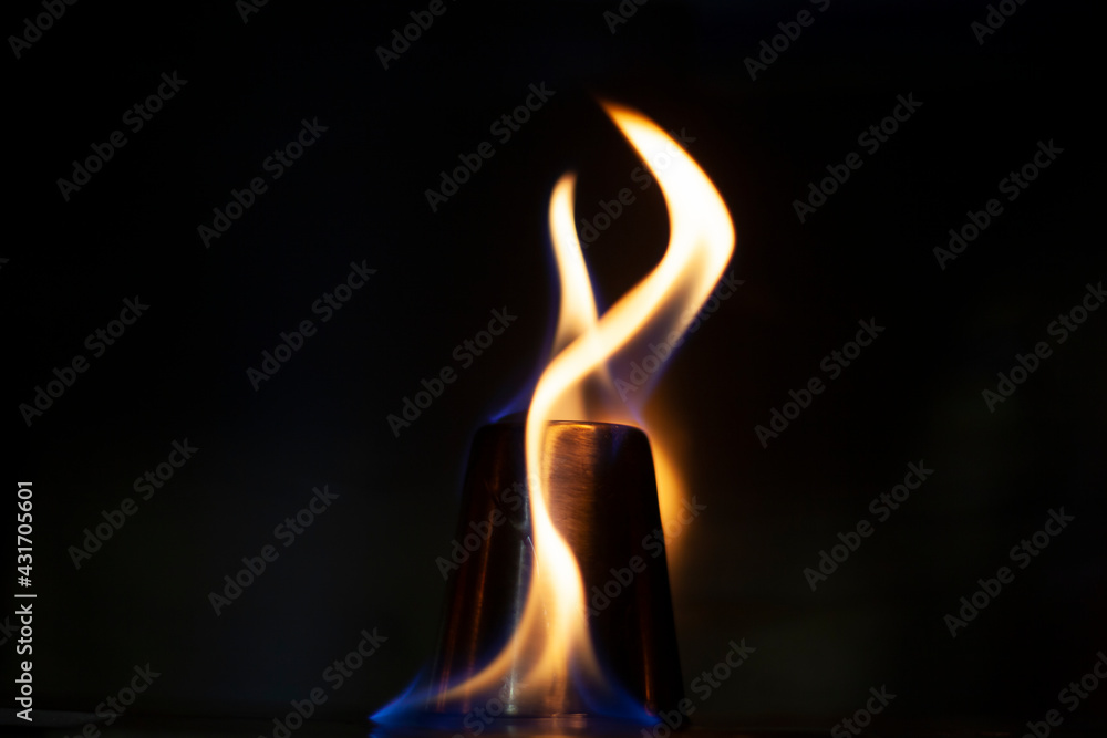 Burning alcohol. Dark background with tongues of flame. Alcohol inflammation. Fire on metal. Two tongues of flame. Preparation for drinking a strong alcoholic drink. Fire blue and orange.