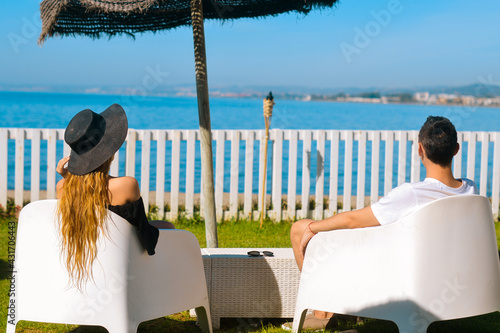 Lovers sitting, looking into sky and sea, mountion, under sun umbrella. Vacation, tourism, hooneymoon. Girl with a long hair. photo