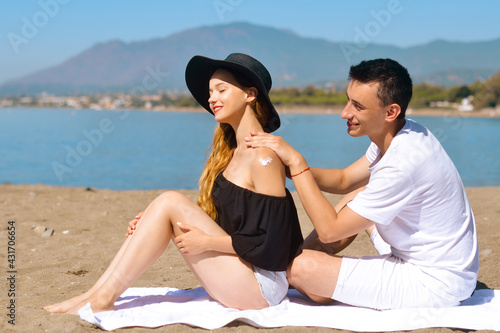 Suncare couple on a summer beach vacation have good skincare with high spf sunblock. Couple applying suncream. Handsome man putting sun tan lotion on his girlfriend at the beach. Vacation, tourism.