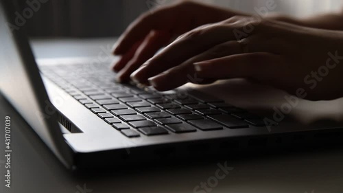 Female hands of a business woman using text input on the keyboard of a silver gray laptop, sitting at a home or office table. Working online concept, close-up 