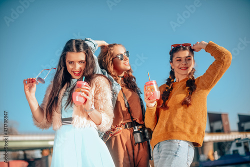 Three girls near the river against the sky having fun. Fashion girls in sunglasses. Jump, rejoice, drink drinks, smile have fun, going crazy. Color dressed friends spend summer vibes, dance