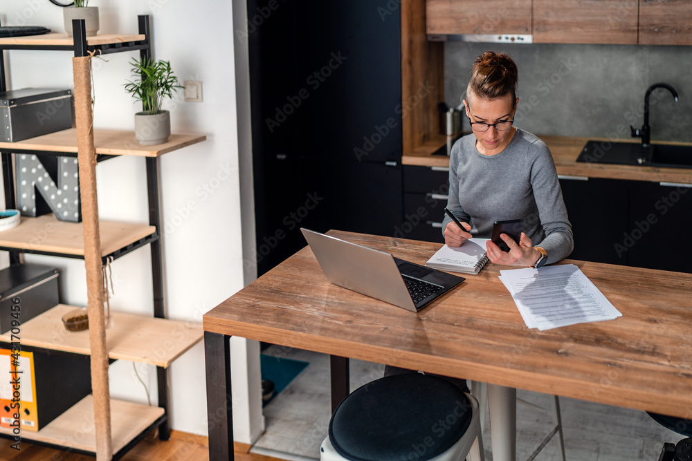 Woman reads messages on her phone while working from home. Woman reads messages on her phone while working from home.