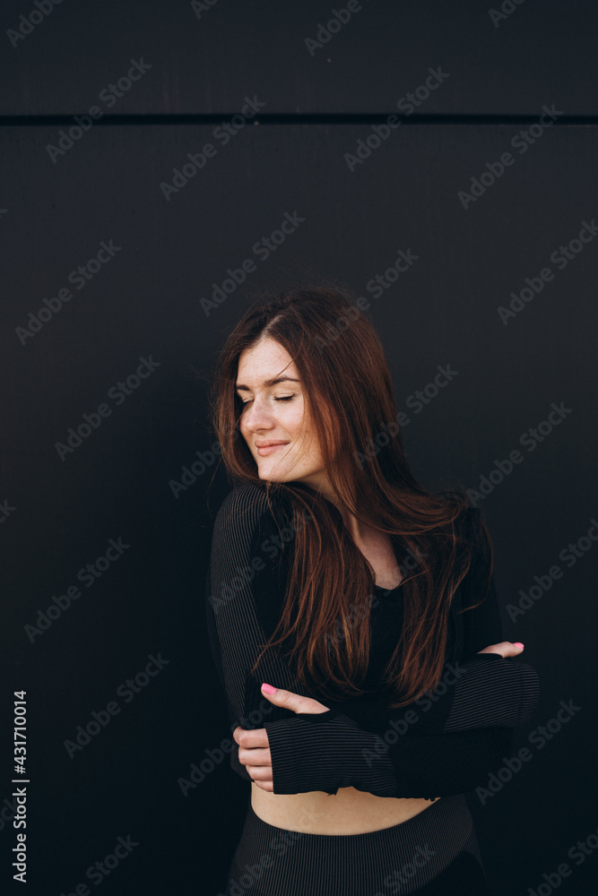Front view of a dreamy fit young woman in active wear leaning against a wall outdoors Front view of a dreamy fit young woman in active wear leaning against a wall outdoors